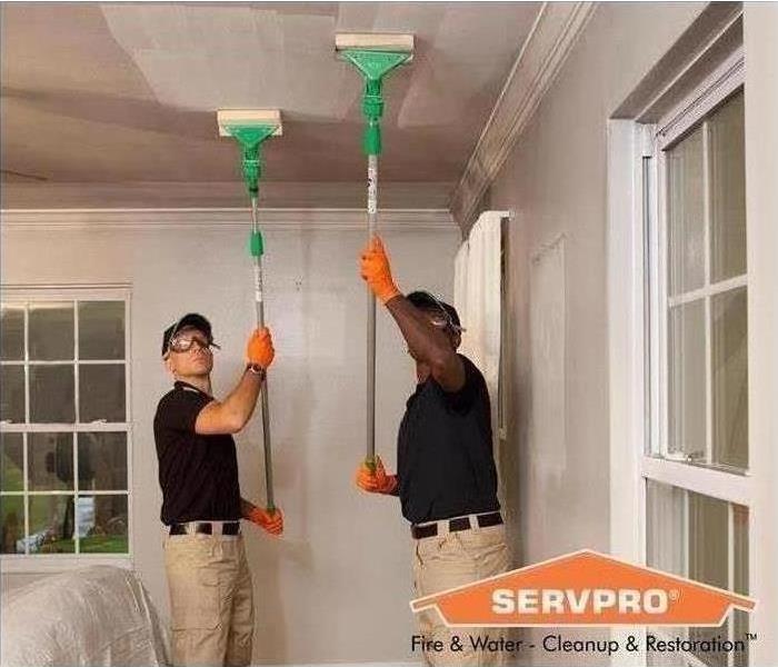 two servpro workers in uniform cleaning ceiling with pole instruments